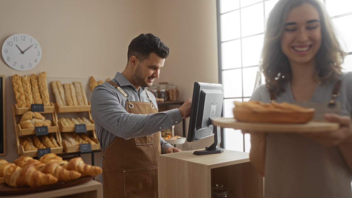 Caisse enregistreuse tactile dans une boulangerie. Une cliente tient dans ses mains une pâtisserie.