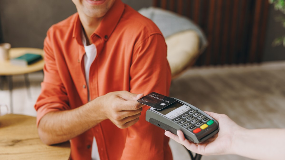 Un client dans un restaurant paie avec une carte bancaire sans contact sur un terminal de paiement mobile.