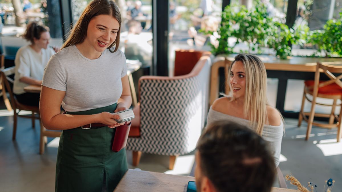 Paiement avec un terminal de paiement mobile dans un restaurant. Une serveuse va présenter le terminal à des clients pour qu'ils puissent payer.