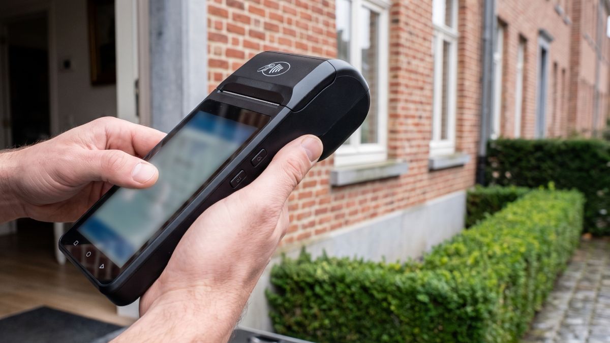 Un terminal de paiement Smile&Pay tenu par un homme devant la maison de clients.