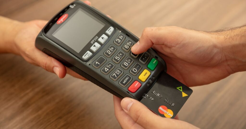 terminal de paiement de la marque ingenico qu'une serveuse tend à un client en train de payer à l'aide de sa carte de crédit mastercard