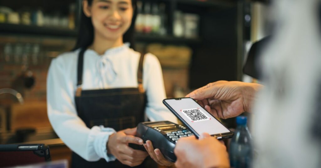 client d'un restaurant en train de payer sa facture à l'aide de son smartphone et d'un qr code repris sur un terminal de paiement électronique sans fil